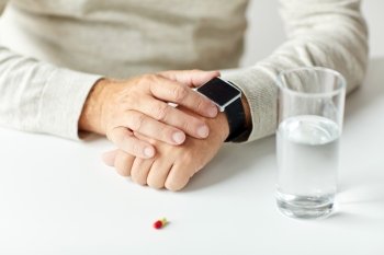 age, medicine, health care and people concept - close up of senior man with glass of water and pill looking at wristwatch