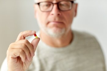 age, medicine, healthcare and people concept - close up of senior man with pill