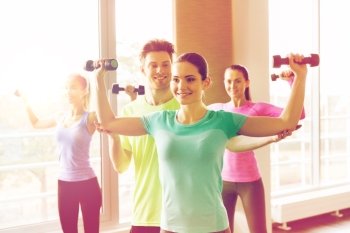 fitness, sport, training and exercising concept - group of smiling people working out with dumbbells flexing muscles in gym