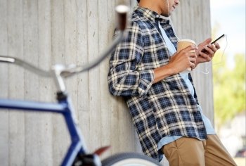 people, technology, leisure and lifestyle - close up of young hipster man with earphones, smartphone and bicycle listening to music