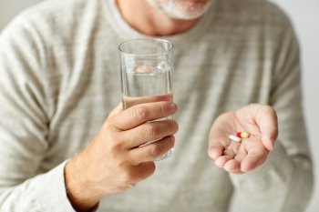 age, medicine, healthcare and people concept - close up of senior man hands with pills and water