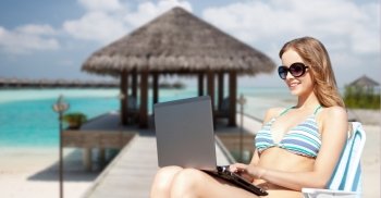 summer holidays, vacation, technology, people and internet - happy young woman in shades with laptop computer over exotic tropical beach and bungalow shed background