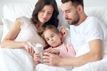 people, family and morning concept - happy child with toy rabbit and parents in bed at home