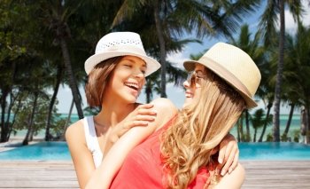 summer holidays, travel, people and vacation concept - happy young women in hats over exotic tropical beach with palm trees and pool background