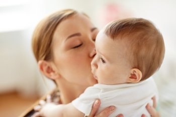 family, child and parenthood concept - close up of happy smiling young mother kissing little baby at home