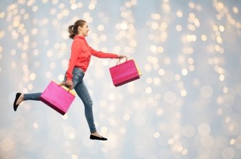 sale, motion and people concept - smiling young woman with shopping bags running in air over holidays lights background. smiling young woman with shopping bags running