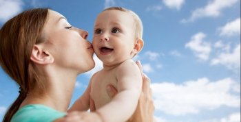 family, child and parenthood concept - close up of happy smiling young mother kissing little baby over blue sky and clouds background. happy mother kissing little baby over blue sky