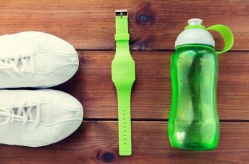 sport, fitness, healthy lifestyle and objects concept - close up of sneakers, bracelet and water bottle on wooden floor. close up of sneakers, bracelet and water bottle