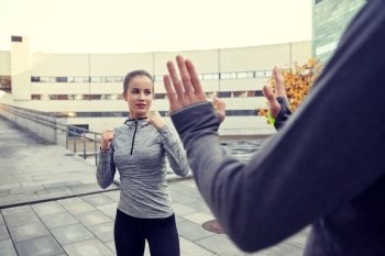 fitness, sport, people, exercising and martial arts concept - young woman with trainer working out self defense strike on city street. woman with trainer working out self defense strike