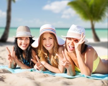 summer holidays, travel, people and vacation concept - happy young women in bikinis sunbathing over exotic tropical beach with palm trees and sea shore background. happy young women in bikinis on summer beach