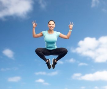 sport, fitness, motion, gesture and people concept - happy smiling young woman jumping in air and showing ok hand sign over blue sky background. happy smiling sporty young woman jumping in air