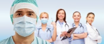 surgery, healthcare, medicine and people concept - surgeon in mask over group of medics on blue background. surgeon in mask with group of medics over blue
