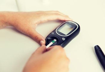 medicine, diabetes, glycemia, health care and people concept - close up of woman hands with glucometer and test stripe checking blood sugar level at home. close up of woman making blood test by glucometer