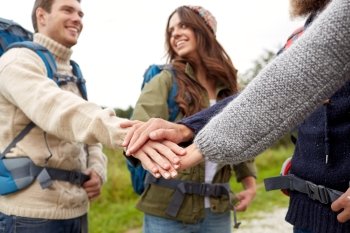 travel, tourism, hike, gesture and people concept - group of smiling friends with backpacks putting hands on top of each other. group of happy friends with backpacks hiking