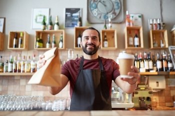 small business, people, takeaway and service concept - happy man or waiter in apron holding coffee cups and paper bag at bar. man or waiter with coffee and paper bag at bar