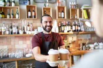 small business, people, takeaway and service concept - happy man or waiter giving paper cup with hot drink to customer at coffee shop. man or waiter serving customer in coffee shop
