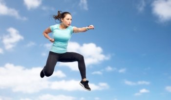 sport, fitness, motion and people concept - happy young woman jumping in air in fighting pose over blue sky background. sporty woman jumping in fighting pose over sky