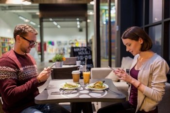 technology, eating, vegetarian food and people concept - happy couple or friends with smartphones having dinner at vegan restaurant. happy couple with smartphones at vegan restaurant