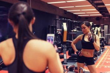 sport, fitness, lifestyle, technology and people concept - young woman with smartphone taking mirror selfie in gym. woman with smartphone taking mirror selfie in gym