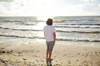 people, leisure and nature concept - young man on summer beach looking at sea. young man on summer beach looking at sea