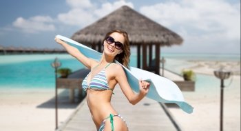 people, summer holidays and vacation concept - beautiful woman in bikini and sunglasses with towel over exotic tropical beach with palm trees background. woman in bikini and sunglasses with towel on beach