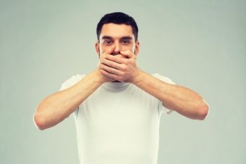 emotion, silence and people concept - man in white t-shirt covering his mouth with hands over gray background. man in white t-shirt covering his mouth with hands
