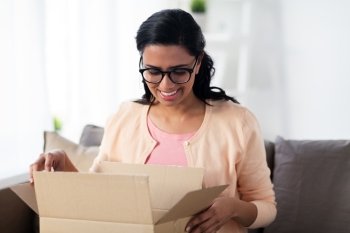 people, delivery, shipping and postal service concept - happy young indian woman holding open cardboard box or parcel at home. happy young indian woman with parcel box at home