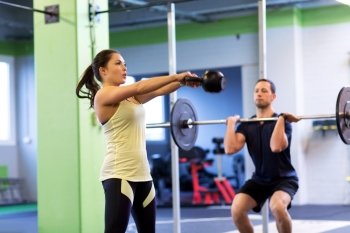 sport, fitness, weightlifting, lifestyle and people concept - man and woman with kettlebell and barbell exercising in gym. man and woman with weights exercising in gym