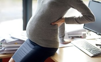 pregnancy, business, work and people concept - pregnant businesswoman sitting on table at office. pregnant businesswoman sitting on table at office