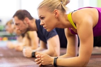 fitness, sport, exercising, people and healthy lifestyle concept - close up of woman with heart-rate tracker at group training doing plank exercise in gym. close up of woman at training doing plank in gym