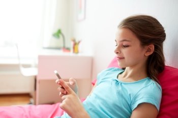 children, technology, people and communication concept - smiling girl texting on smartphone or playing game at home. smiling girl texting on smartphone at home