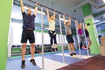 sport, fitness, exercising and training concept - group of people hanging at horizontal bar in gym. group of people hanging at horizontal bar in gym