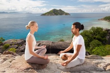 fitness, sport, meditation and people concept - happy couple doing yoga and meditating outdoors over natural background and sea. happy couple doing yoga and meditating outdoors