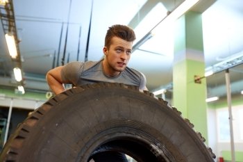 strongman, bodybuilding, sport, fitness and people concept - young man doing tire flip at training in gym. man doing strongman tire flip training in gym