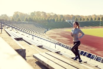 fitness, sport, exercising and people concept - happy young woman running upstairs on stadium. happy young woman running upstairs on stadium