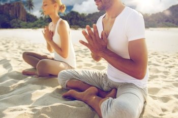 fitness, sport, people and yoga concept - close up of couple meditating in lotus pose outdoors over exotic tropical beach background. close up of couple making yoga exercises outdoors