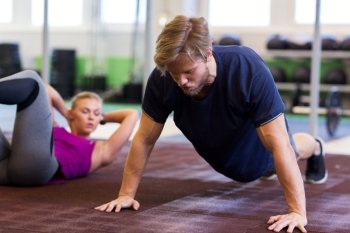 fitness, sport, training, exercising and people concept - woman doing push ups or straight arm plank  in gym. man exercising and doing straight arm plank in gym