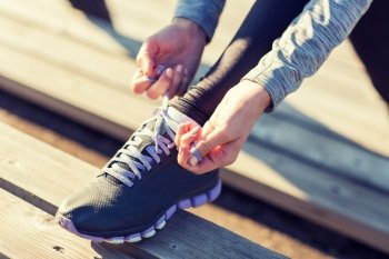 fitness, sport, people and lifestyle concept - close up of young sporty woman tying shoelaces outdoors. close up of sporty woman tying shoelaces outdoors