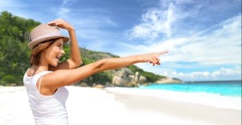 summer holidays, travel, people and vacation concept - happy smiling young woman in hat pointing finger over exotic tropical beach with palm trees and sea shore background. happy young woman in hat on summer beach