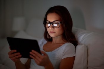 technology, vision, communication and people concept - young woman in glasses with tablet pc computer in bed at home bedroom at night. woman with glasses and tablet pc in bed at home