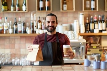 small business, people, takeaway and service concept - happy man or waiter in apron holding coffee cups and paper bag at bar. man or waiter with coffee and paper bag at bar