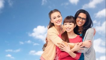 diversity, friendship and people concept - international group of happy smiling different women hugging over blue sky and clouds background. international group of happy women hugging