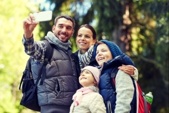 travel, tourism, hike, technology and people concept - happy family with backpacks taking selfie by smartphone in woods. family taking selfie with smartphone in woods