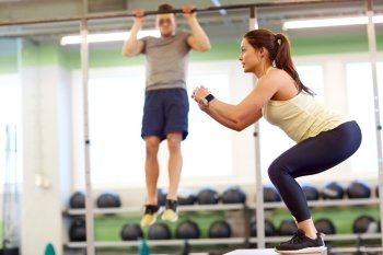 fitness, sport, training, exercising and people concept - woman and man doing pull-ups and box jumps in gym. woman and man exercising in gym