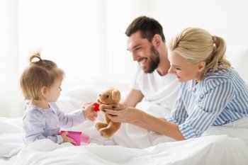 people, family, holidays and morning concept - happy little girl and parents with gift box in bed at home. happy family with gift box in bed at home