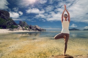 fitness, sport, people and recreation concept - young woman making yoga tree pose from back over exotic tropical beach background. young woman making yoga tree pose over beach