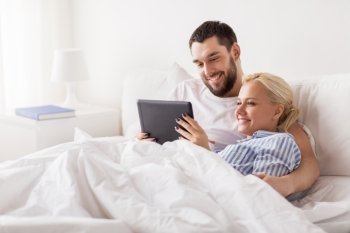 family, technology, internet and people concept - smiling happy couple with tablet pc computer in bed at home bedroom. smiling happy couple with tablet pc in bed at home