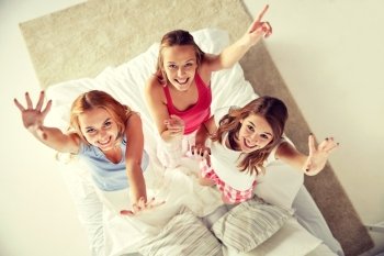 friendship, people and pajama party concept - happy friends or teenage girls having fun, dancing and jumping on bed at home. happy friends or teen girls having fun at home