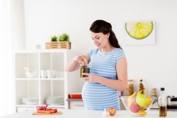 pregnancy, nutrition and people concept - happy pregnant woman eating pickles at home kitchen. pregnant woman eating pickles at home kitchen