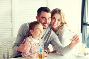 family, parenthood, technology and people concept - happy mother, father and little girl having dinner and taking selfie by smartphone at restaurant. happy family taking selfie at restaurant